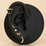 A black mannequin ear displays 14K Recycled Solid Yellow Gold Twisted Huggie Earrings among other gold styles against a beige background.