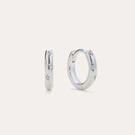 Starfall Huggies in Silver, a pair of sterling silver hoop earrings featuring engraved star motifs with small embedded stones.