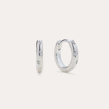 Starfall Huggies in Silver, a pair of sterling silver hoop earrings featuring engraved star motifs with small embedded stones.