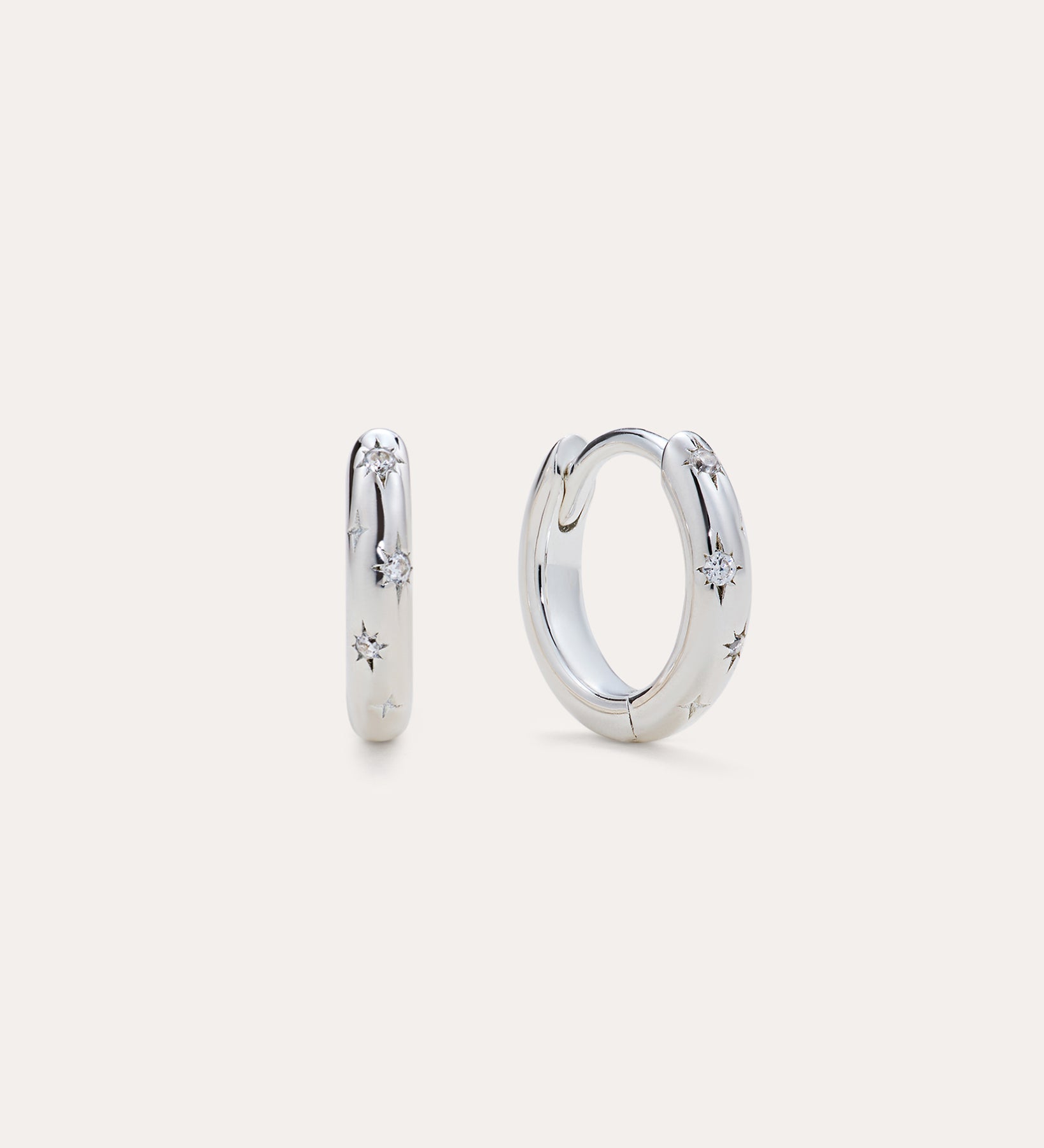 Starfall Huggies in Silver, a pair of sterling silver hoop earrings featuring engraved star motifs with small embedded stones.