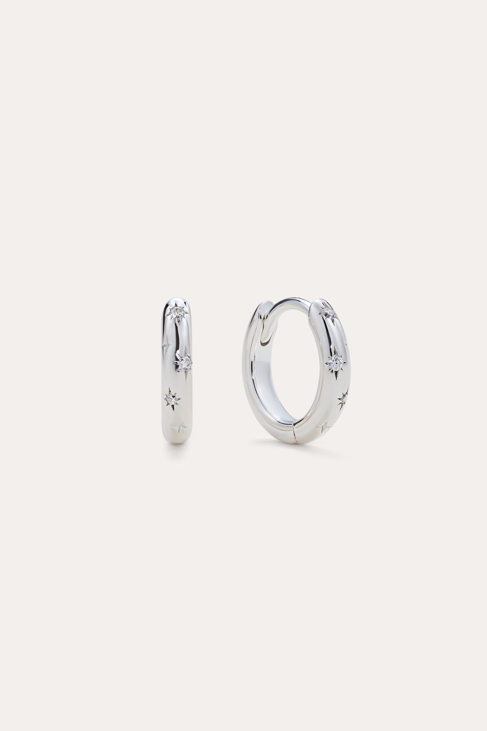 Starfall Huggies in Silver, a pair of sterling silver hoop earrings featuring engraved star motifs with small embedded stones.