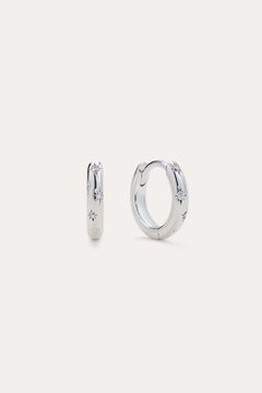 Starfall Huggies in Silver, a pair of sterling silver hoop earrings featuring engraved star motifs with small embedded stones.