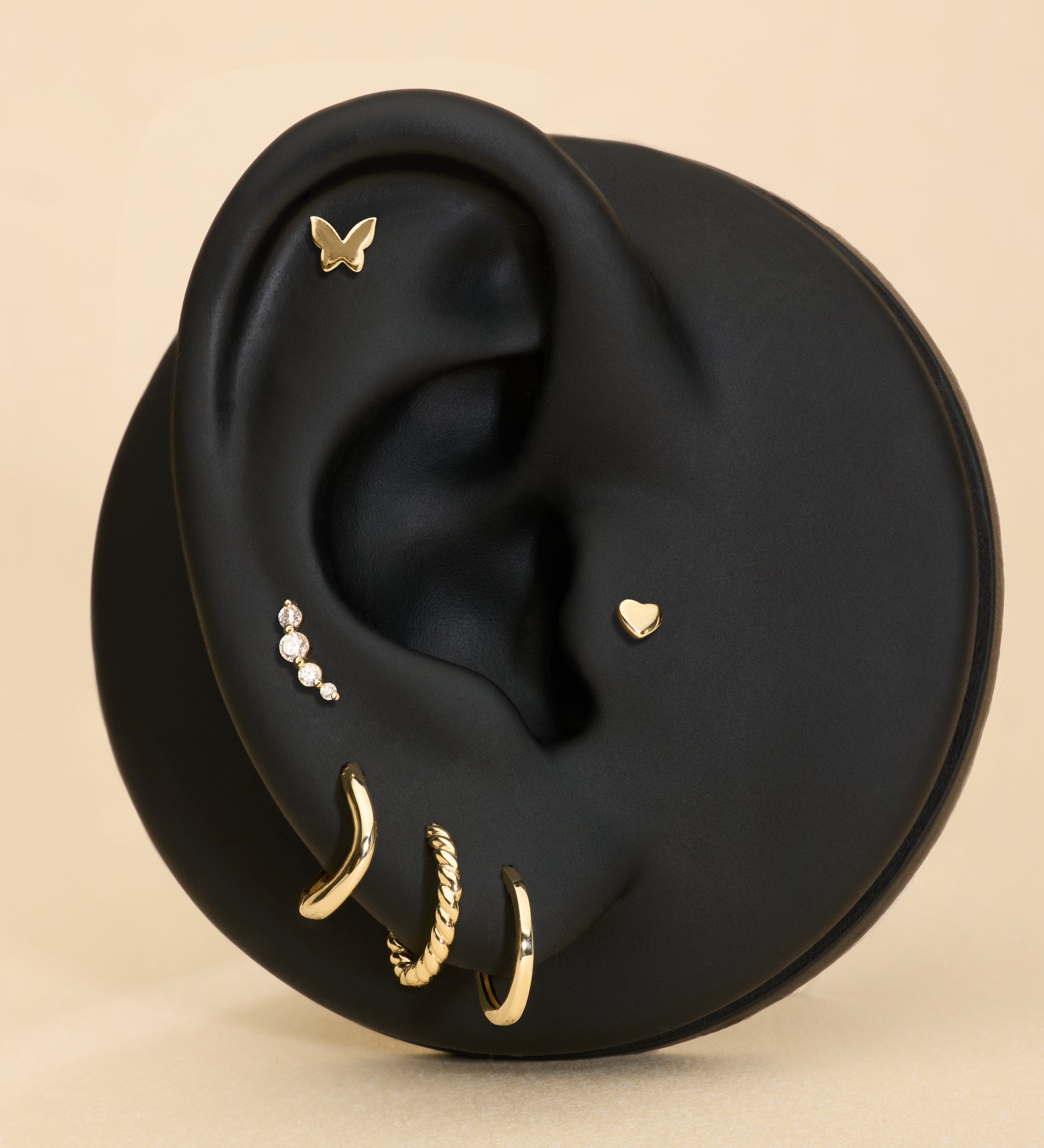 Black ear with gold earrings, butterfly flatback studs, heart flatback and diamond a beige background