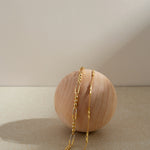 The Bamboo Chain Bracelet in Gold, featuring a delicate 18k gold-plated design, is elegantly displayed draped over a smooth, light wooden sphere against a neutral beige background with soft lighting and gentle shadows.