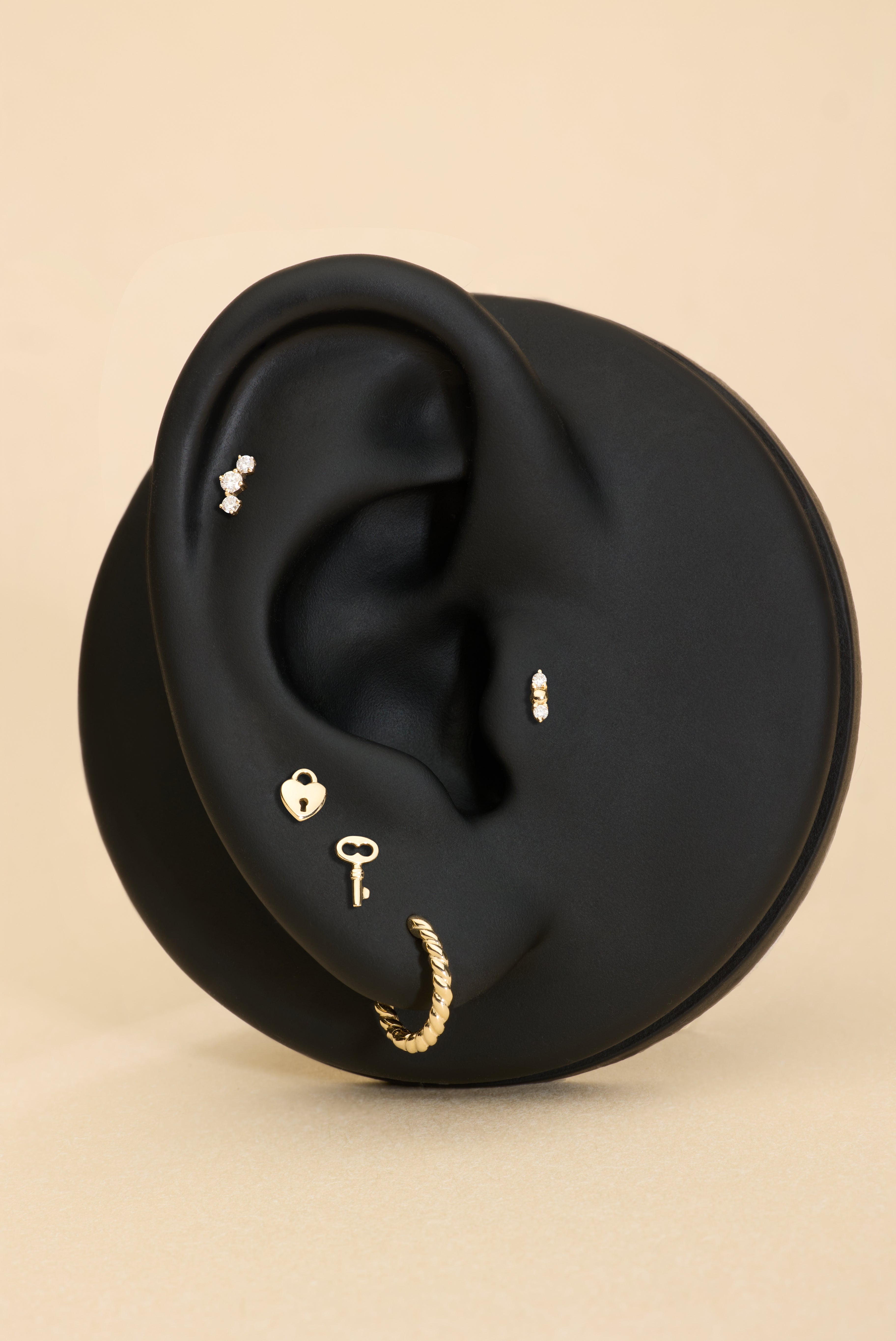 A black ear-shaped jewelry display features the 14K Solid Yellow Gold Lab-Grown Diamond Curved Trio Flat Back Stud along with four other gold and diamond earrings, all set against a beige background.