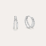 The Mae Twist Double Huggie Earrings in Silver feature a twisted, leafy design. Displayed on a plain background, one earring stands slightly open while the other lies flat, showcasing their intricate detailing.