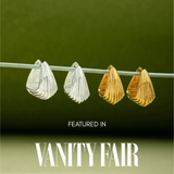 A pair of Juno Ridged Chunky Hoops in Silver hangs on a clear rod against a green gradient background. Text below reads, Featured in Vanity Fair.