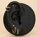 Gold earrings displayed on a black ear with a beige background