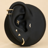 A black ear-shaped display showcases the 14K Solid Yellow Gold Snake Flat Back Stud among other gold earrings and studs—ideal for helix piercings—set against a beige background.