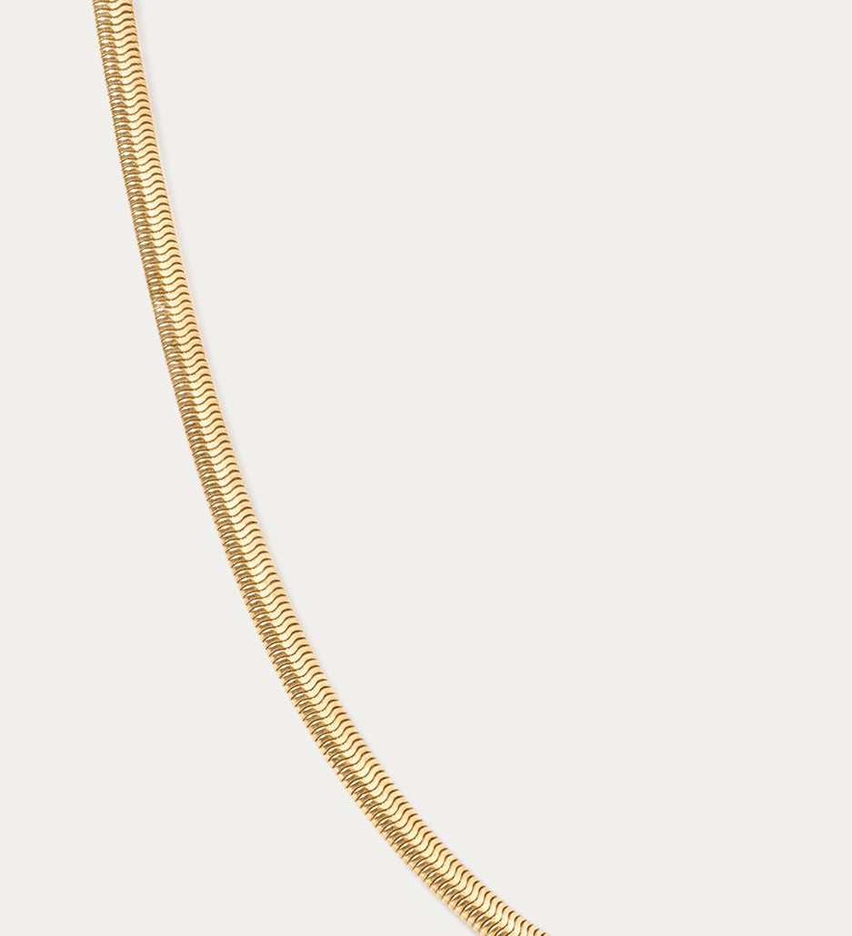 The Estelle Herringbone Chain Necklace in Gold is displayed against a plain white background, featuring a sleek 3mm chain for timeless elegance.
