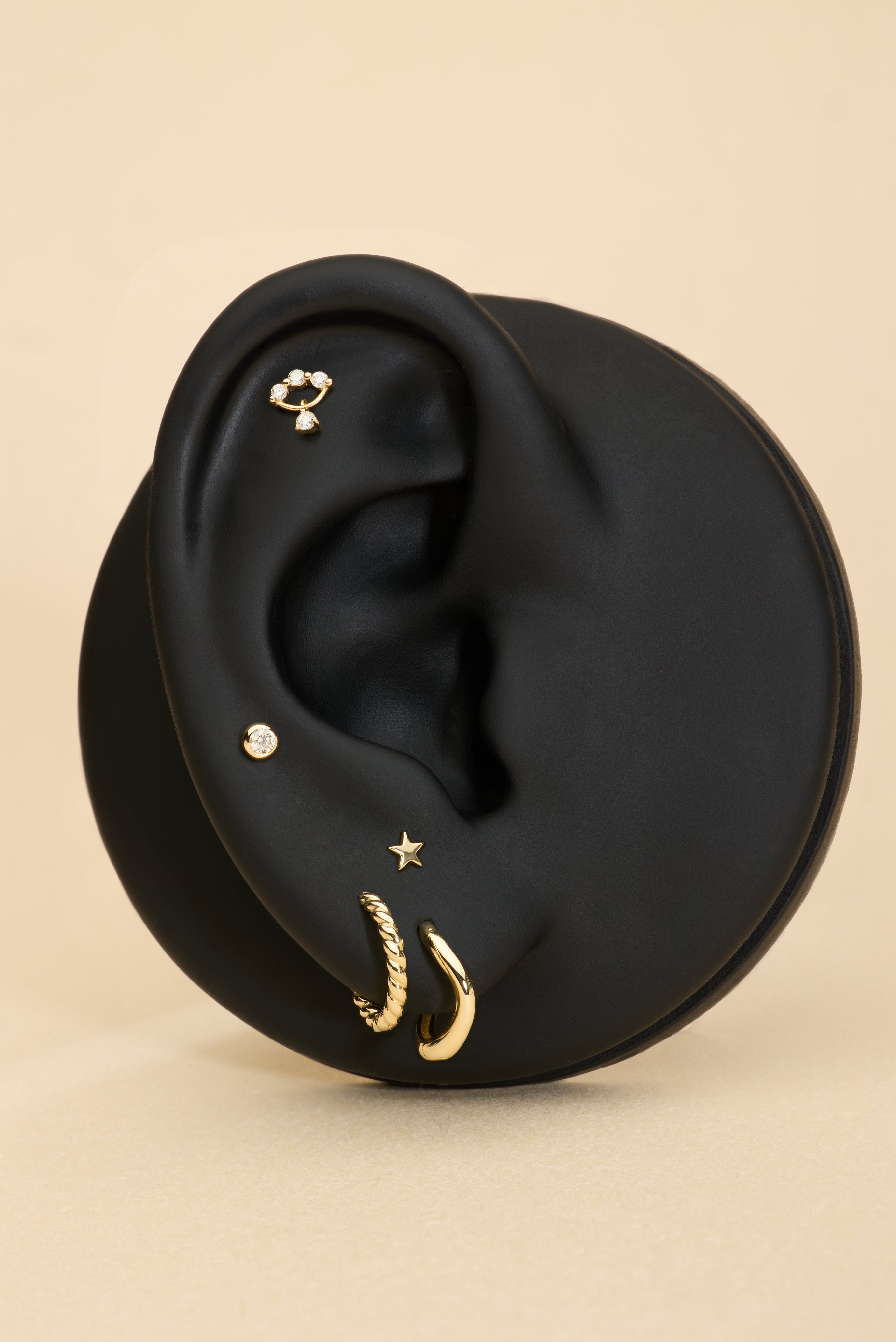 Black ear with gold earrings on a beige background with solid gold flatback studs
