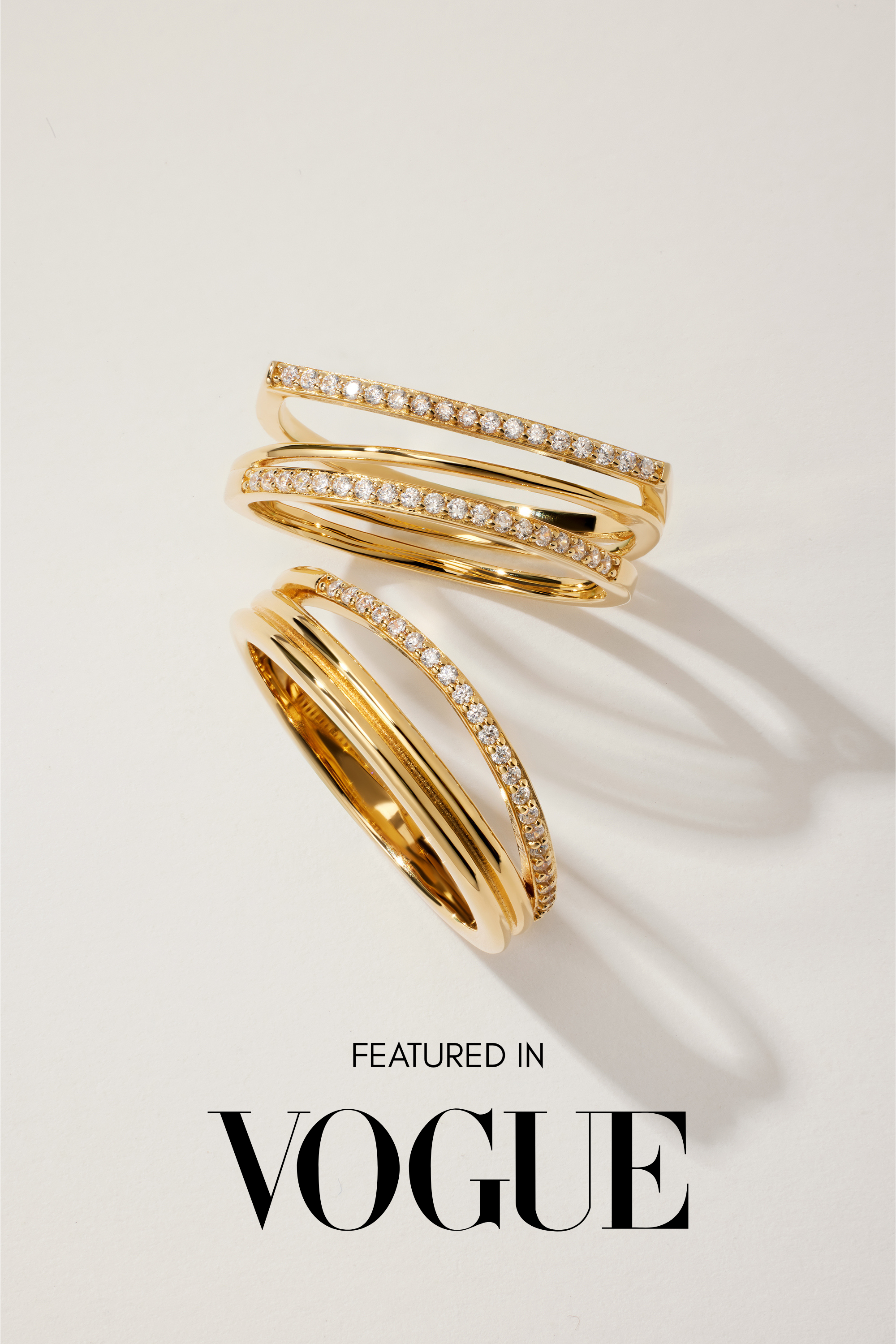 The Noor Pavé Triple Band Rings in Gold, featuring rows of sparkling pavé diamonds, are displayed on a white surface with soft shadows. Below the rings, the text reads Featured in VOGUE.