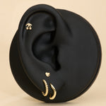 Black ear with gold stud cherry earrings and gold heart flat back stud on a beige background