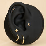 A black ear model showcases the 14K Recycled Solid Yellow Gold Plain Huggie Earring and other sustainable jewelry, set against a beige background.