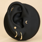 A black ear model showcases the 14K Recycled Solid Yellow Gold Plain Huggie Earring and other sustainable jewelry, set against a beige background.