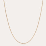 The Alba Tennis Necklace in Gold features a thin, simple design with fine links and a subtle shine, shown in a gentle curve against a light background.