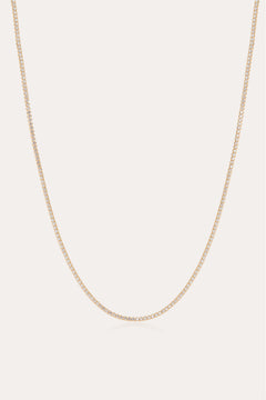 The Alba Tennis Necklace in Gold features a thin, simple design with fine links and a subtle shine, shown in a gentle curve against a light background.