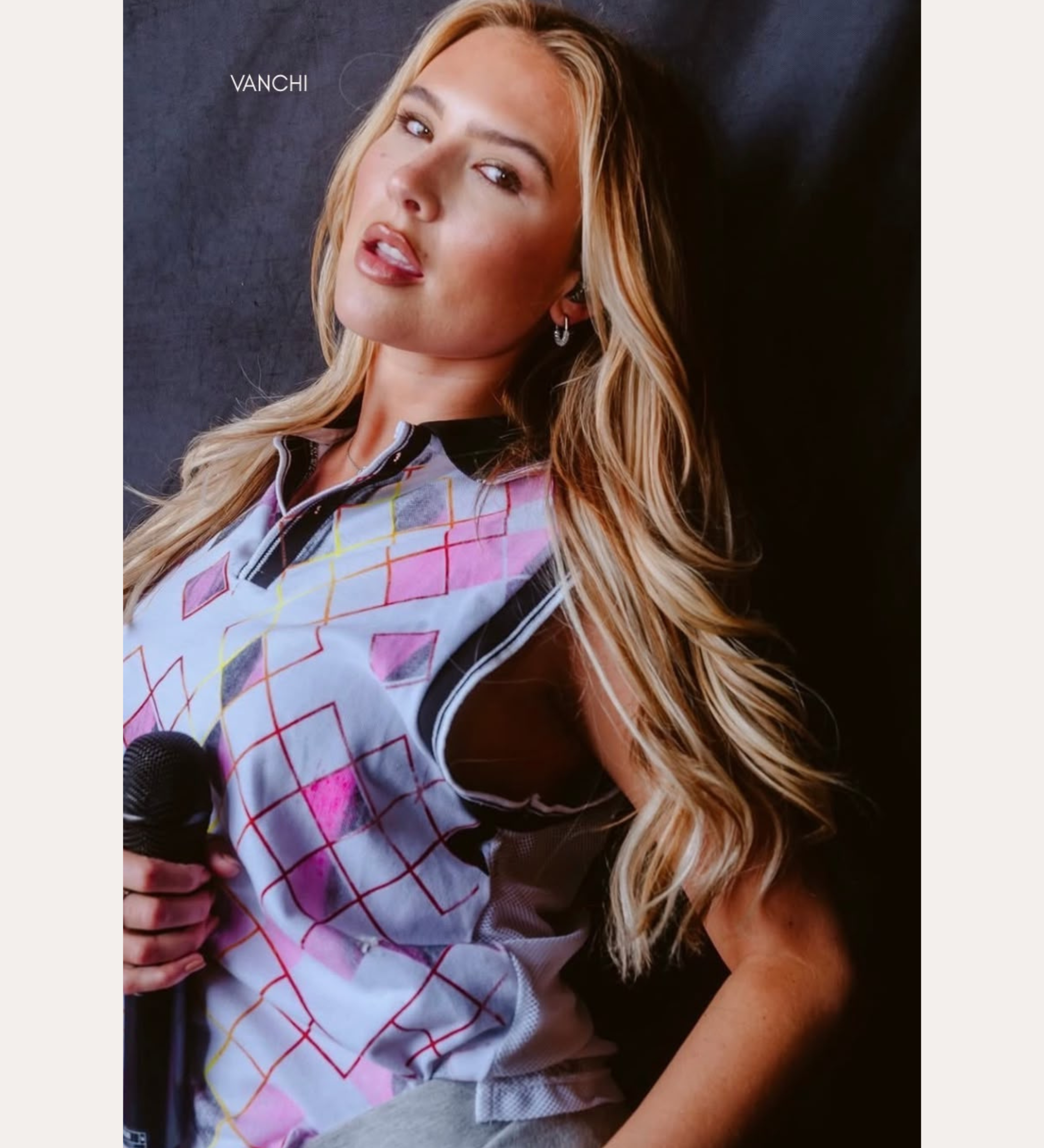 A woman with long blonde hair holds a microphone, wearing a colorful sleeveless top with a grid pattern and the elegant Nouf Pavé Hoop Earrings in Gold, crafted from 18k gold plated metal and sparkling cubic zirconia. The background is plain, with text above her reading “SPOTTED ON:” and below, “MIMI WEBB.”.