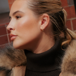 Profile view of a person wearing a small 18k gold plated Georgie Crystal Knife Edge Huggie Hoop Earrings with crystal accents.