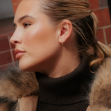 Profile view of a person wearing a small 18k gold plated Georgie Crystal Knife Edge Huggie Hoop Earrings with crystal accents.