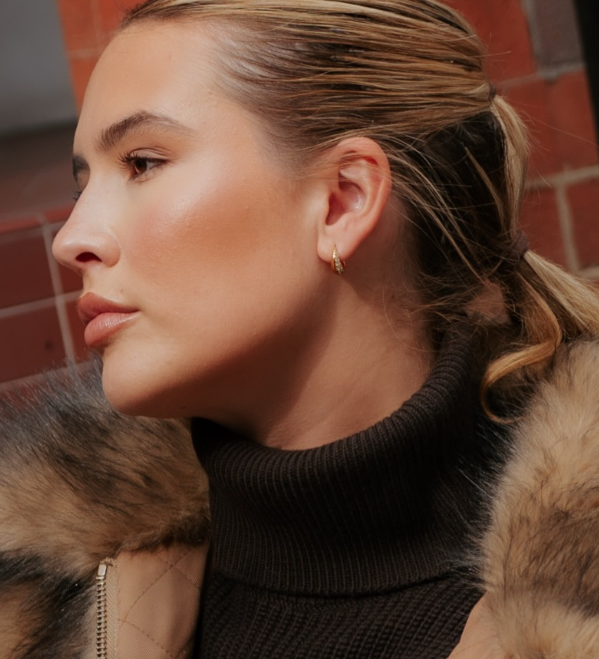 Profile view of a person wearing a small 18k gold plated Georgie Crystal Knife Edge Huggie Hoop Earrings with crystal accents.