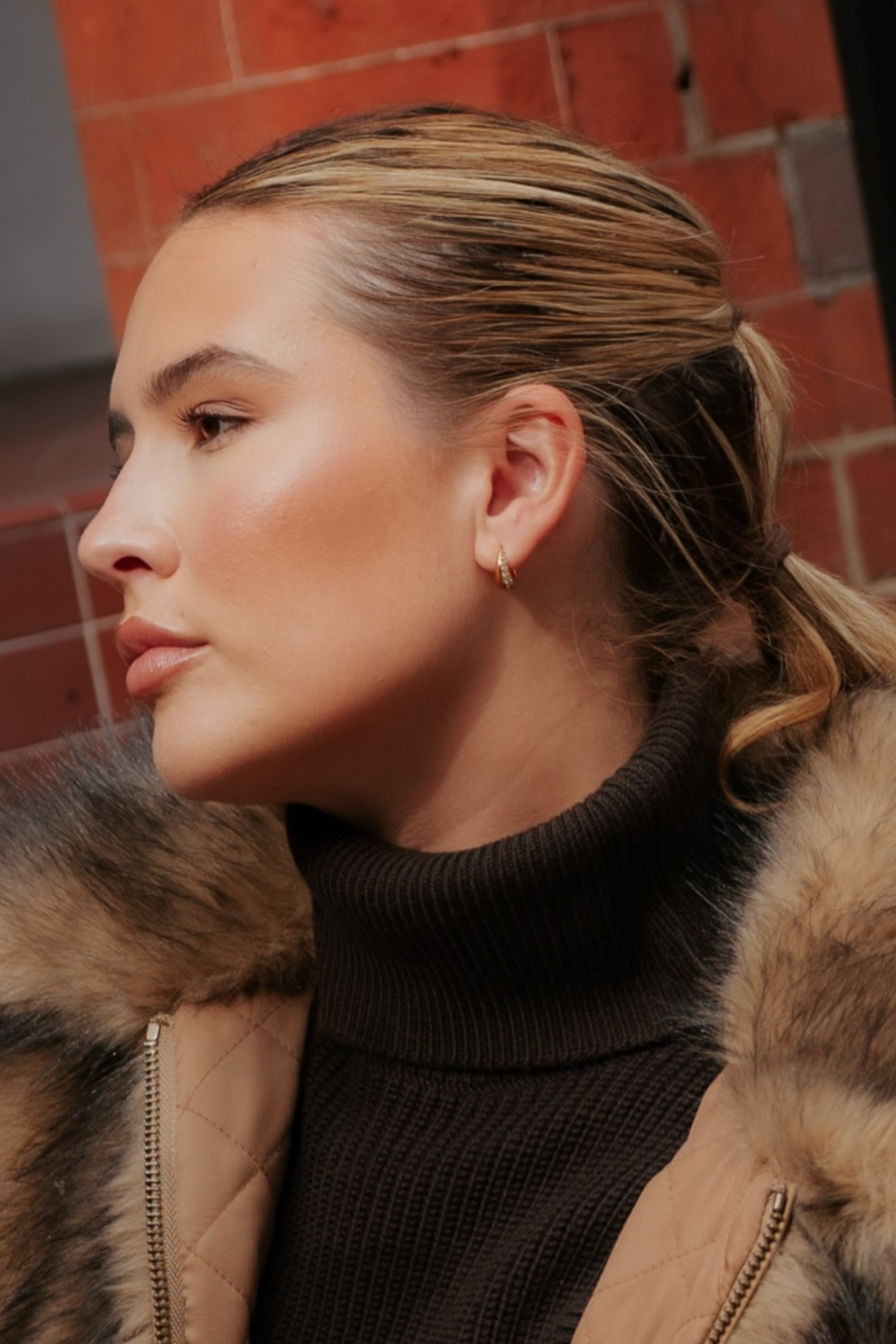 Profile view of a person wearing a small 18k gold plated Georgie Crystal Knife Edge Huggie Hoop Earrings with crystal accents.