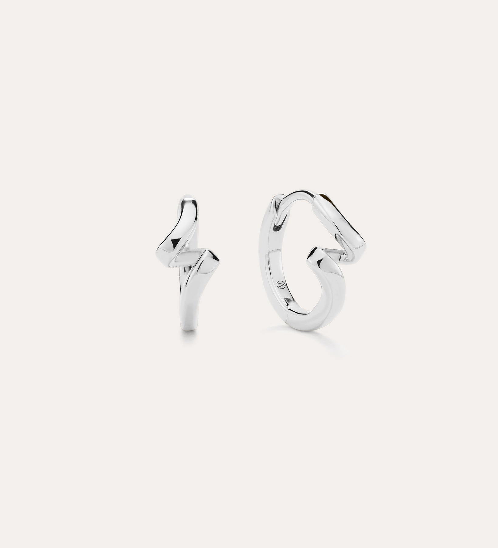 A pair of Ribbon Twist Huggies in sterling silver—one shaped like a lightning bolt, the other with a smooth, twisted ribbon design—are displayed against a plain white background.