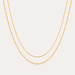 The Figaro And Box Chain Layered Necklace in 18k Gold Plated features a dual design: a sleek box chain above and elongated Figaro links below, beautifully displayed against a white background for an elegant layered look.