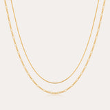 The Figaro And Box Chain Layered Necklace in 18k Gold Plated features a dual design: a sleek box chain above and elongated Figaro links below, beautifully displayed against a white background for an elegant layered look.