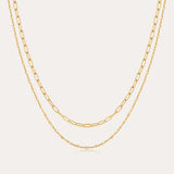 The Mini Paperclip Double Chain Necklace in Gold features two 18k gold plated layered chains—one with delicate elongated links, the other with fine round links—displayed elegantly against a plain, light background.