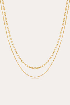 The Mini Paperclip Double Chain Necklace in Gold features two 18k gold plated layered chains—one with delicate elongated links, the other with fine round links—displayed elegantly against a plain, light background.