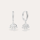 Defender Evil Eye Hoops in Sterling Silver featuring hoops with dangling stylized eye charms, each set with a central clear gemstone and three smaller stones below. Displayed against a light, plain background.