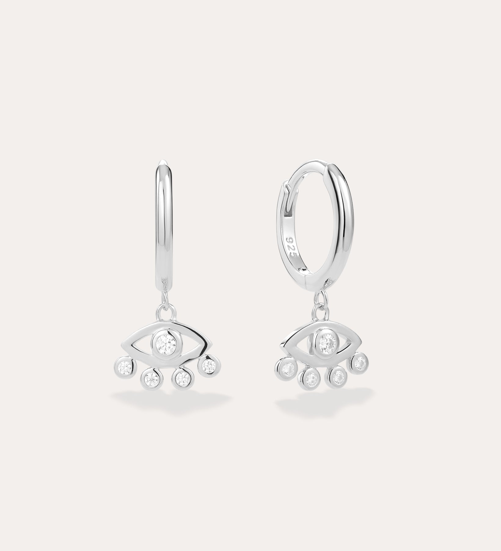 Defender Evil Eye Hoops in Sterling Silver featuring hoops with dangling stylized eye charms, each set with a central clear gemstone and three smaller stones below. Displayed against a light, plain background.