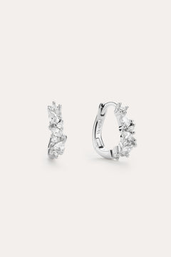 The Nori Twisted Crystal Huggies in Sterling Silver are chic hoops featuring multiple sparkling white crystals, beautifully showcased against a plain, light background.