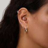 Close-up of a person's ear adorned with multiple earrings, including the Nori Twisted Hoop Earrings in Gold on the lobe. The person has long, dark hair and light brown skin.
