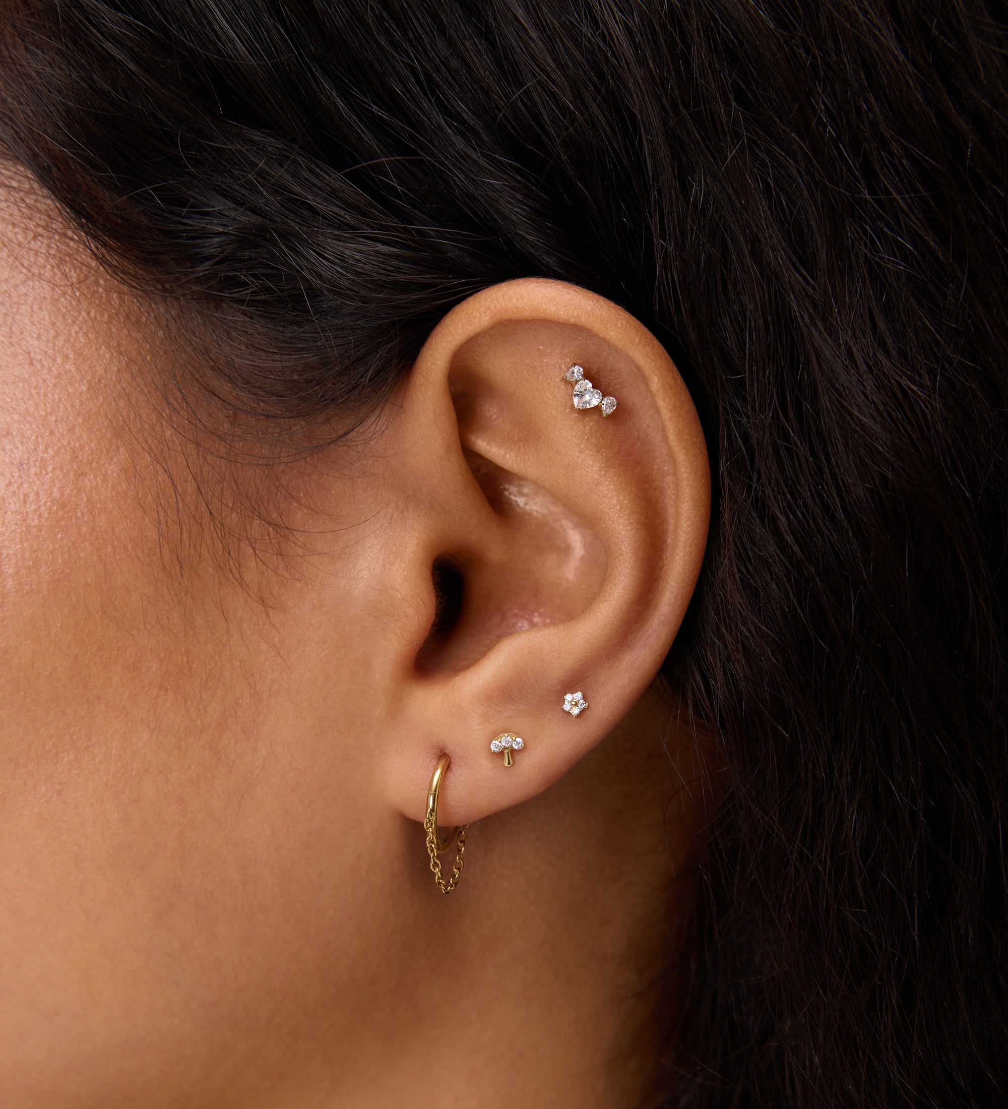 Close-up of a woman's ear adorned with the Chain Clicker Titanium Ring in Gold and multiple studs—an ideal look for highlighting hypoallergenic earrings.