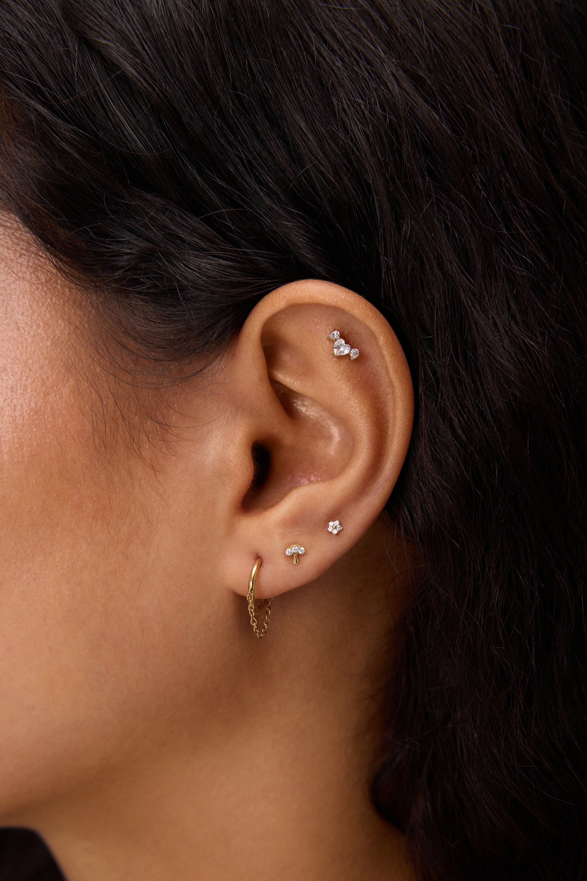 Close-up of a woman's ear adorned with the Chain Clicker Titanium Ring in Gold and multiple studs—an ideal look for highlighting hypoallergenic earrings.