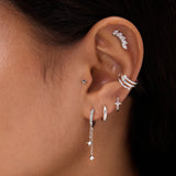 Close-up of a person with dark hair and warm skin tone wearing multiple silver and diamond earrings, including the 14K Solid White Gold Mini Star Flat Back Stud, hoops, dangling chains, and an ear cuff.
