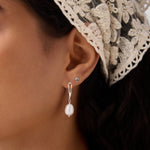 Close-up of a woman's ear wearing the 14K Solid Yellow Gold Shell Flat Back Stud and a silver drop earring with a pearl. She has dark hair, a cream lace headscarf, and a matching pearl necklace partially visible.