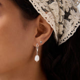 Close-up of a woman's ear wearing the 14K Solid Yellow Gold Shell Flat Back Stud and a silver drop earring with a pearl. She has dark hair, a cream lace headscarf, and a matching pearl necklace partially visible.