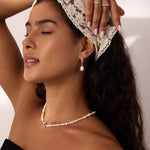 A woman with long dark hair, wearing a lace headscarf, pearl jewelry, and a black top, poses with one arm raised and eyes closed in soft lighting, showcasing the 14K Solid White Gold Shell Flat Back Stud.