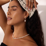 A woman with long dark hair, wearing a lace headscarf, pearl jewelry, and a black top, poses with one arm raised and eyes closed in soft lighting, showcasing the 14K Solid White Gold Shell Flat Back Stud.