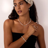 A woman with long dark hair wears a cream lace headscarf, Freshwater Pearl Charm Huggies in Silver, and a black strapless top, standing against a light background and looking to the side with a relaxed expression.
