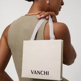 A woman wears the Freshwater Pearl Charm Huggies in Silver with a matching necklace, holding a white VANCHI shopping bag over her shoulder. She is dressed in a sleeveless olive dress and is facing slightly away from the camera.