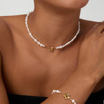 Wearing the Flora Multi Pearl Toggle Choker in Gold, a smiling person showcases its elegant freshwater pearls, delicate gold charm, and sophisticated floral toggle clasp against a plain background.