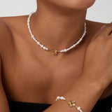 Wearing the Flora Multi Pearl Toggle Choker in Gold, a smiling person showcases its elegant freshwater pearls, delicate gold charm, and sophisticated floral toggle clasp against a plain background.