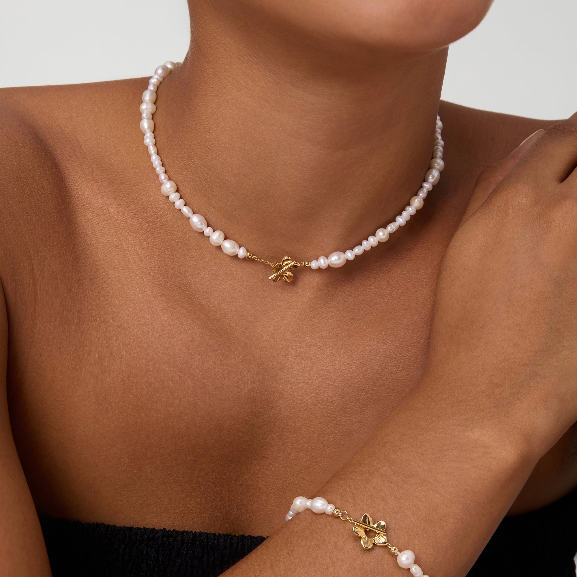 Wearing the Flora Multi Pearl Toggle Choker in Gold, a smiling person showcases its elegant freshwater pearls, delicate gold charm, and sophisticated floral toggle clasp against a plain background.