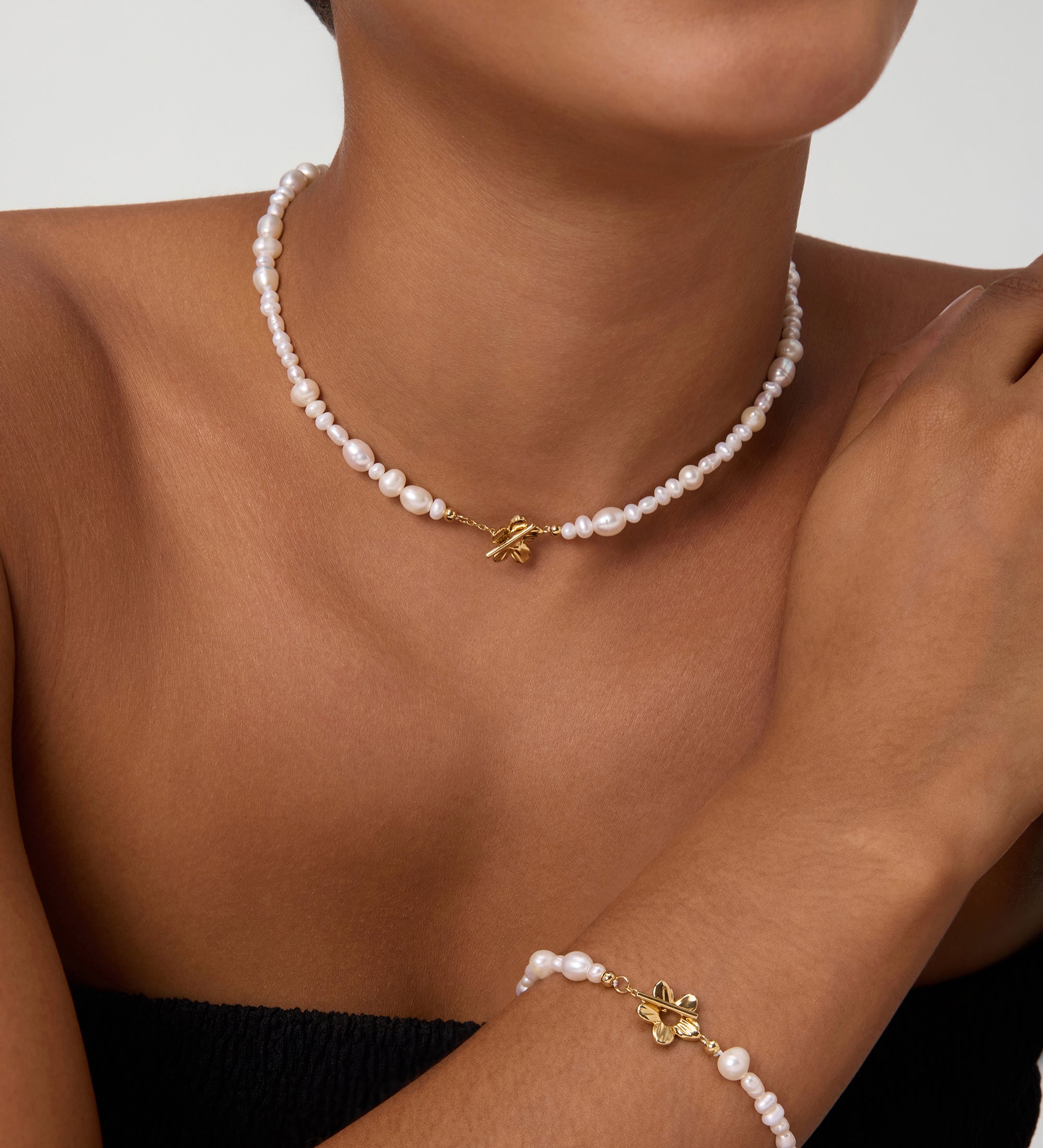Wearing the Flora Multi Pearl Toggle Choker in Gold, a smiling person showcases its elegant freshwater pearls, delicate gold charm, and sophisticated floral toggle clasp against a plain background.