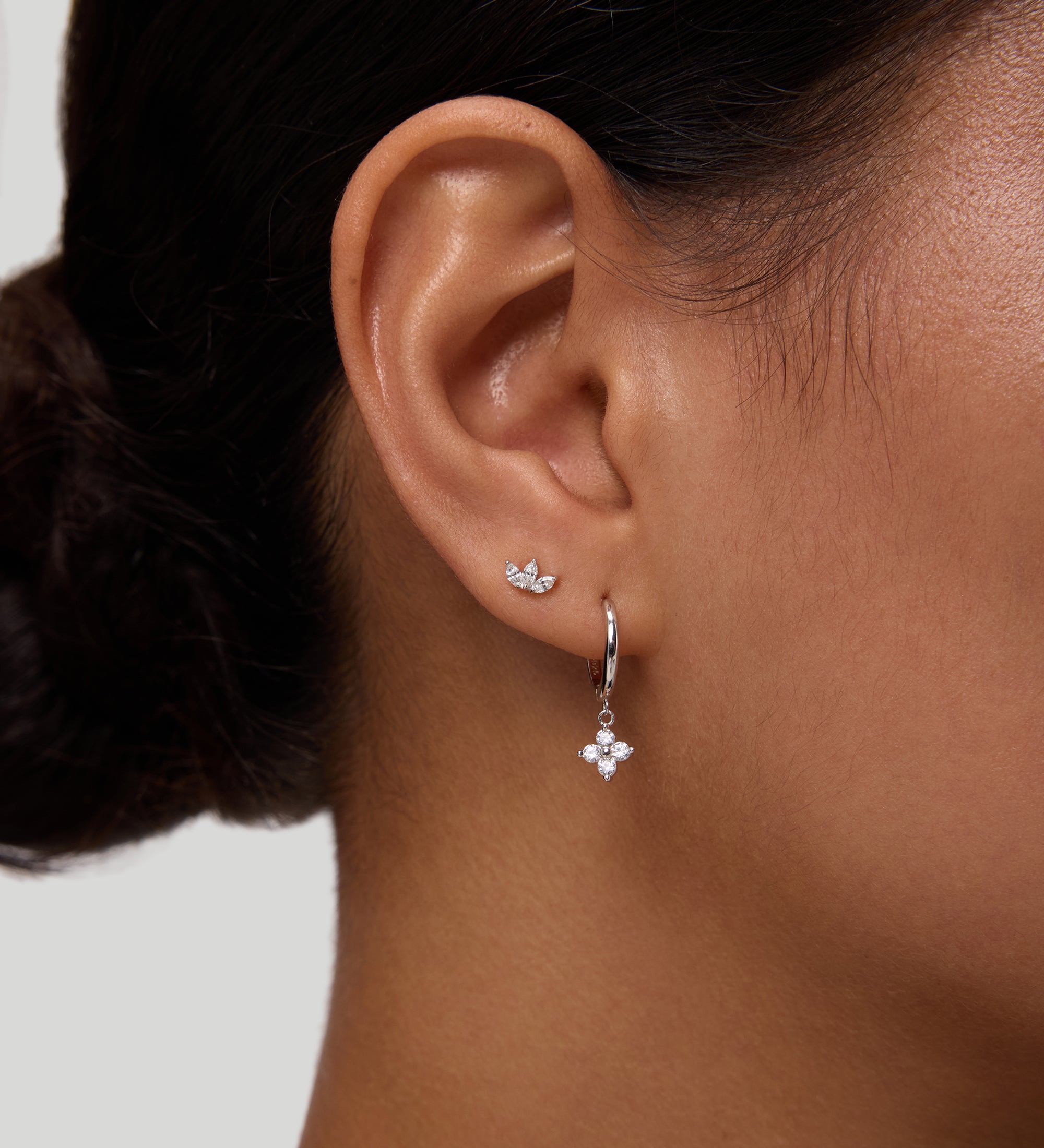 Close-up of a woman's ear wearing the Flora Crystal Charm Huggies in Gold, featuring sparkling cubic zirconia and a gold-plated finish, set against a plain background.
