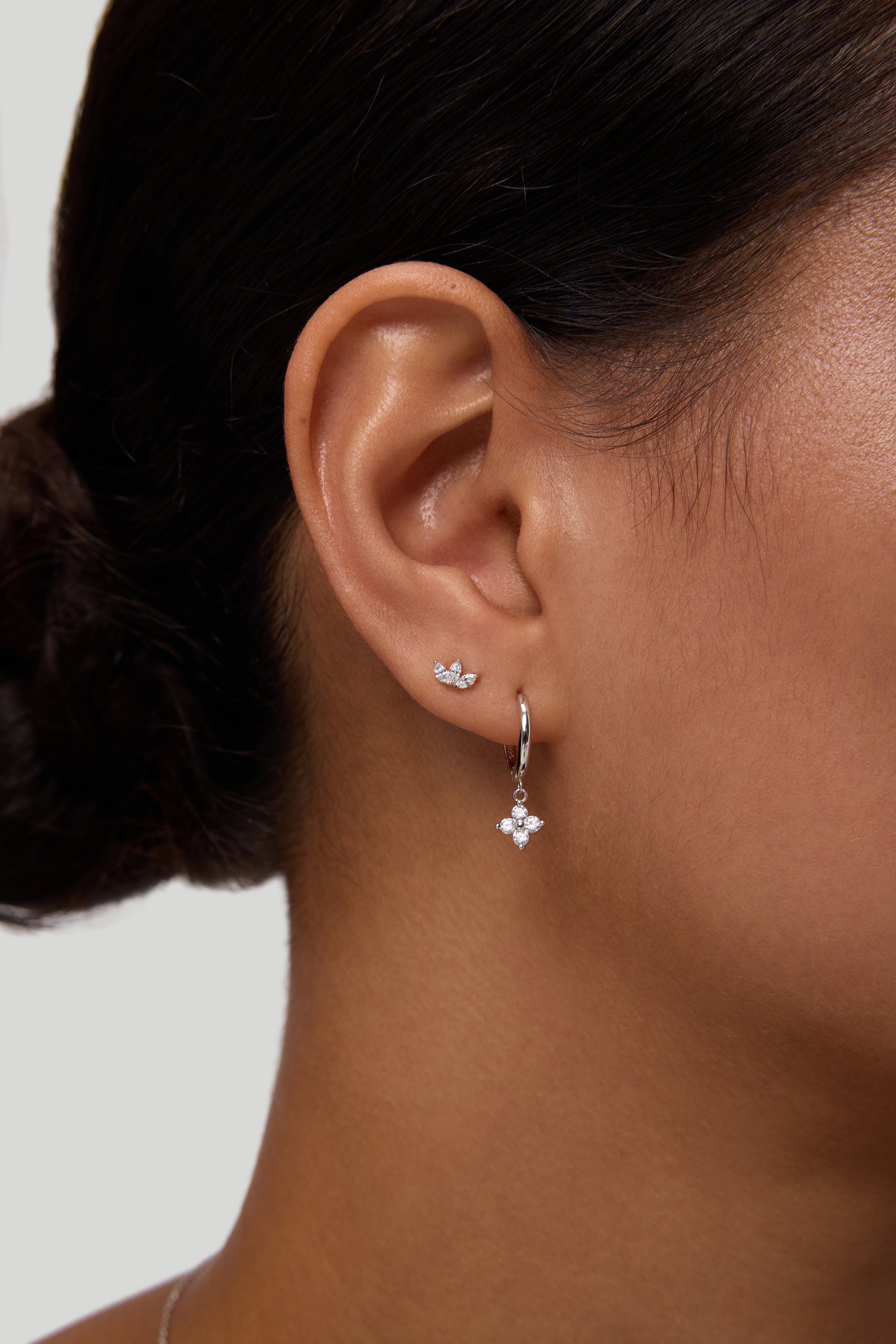 Close-up of a woman's ear wearing the Flora Crystal Charm Huggies in Gold, featuring sparkling cubic zirconia and a gold-plated finish, set against a plain background.